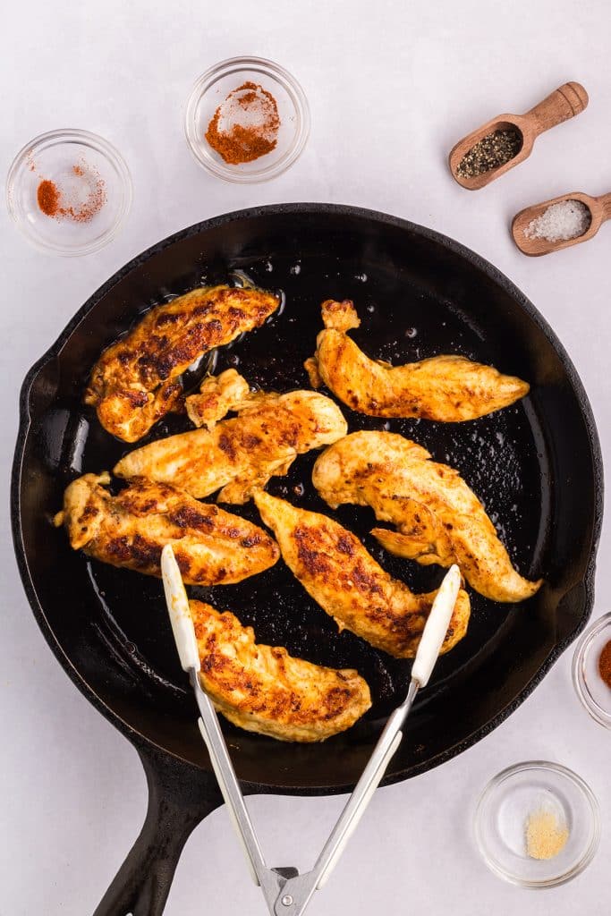chicken in a cast iron skillet with tongs.
