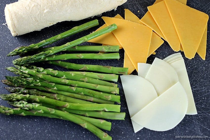 fresh asparagus laid out with sliced cheese for asparagus puffs