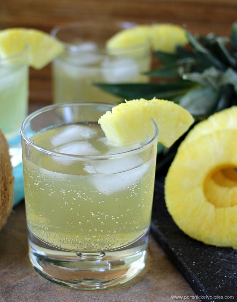 three skinny pineapple coconut cocktails in glasses with fresh pineapple garnishes Skinny Pineapple Coconut Cocktail is a fizzy, low calorie drink that is perfect for summertime. | www.persnicketyplates.com