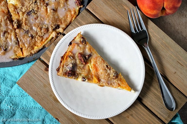 Peach Crumble Fruit Pizza is made on a cake batter crust, piled with thinly sliced fresh peaches and topped with a crumble and pecans and drizzled with a cinnamon sugar glaze. | www.persnicketyplates.com