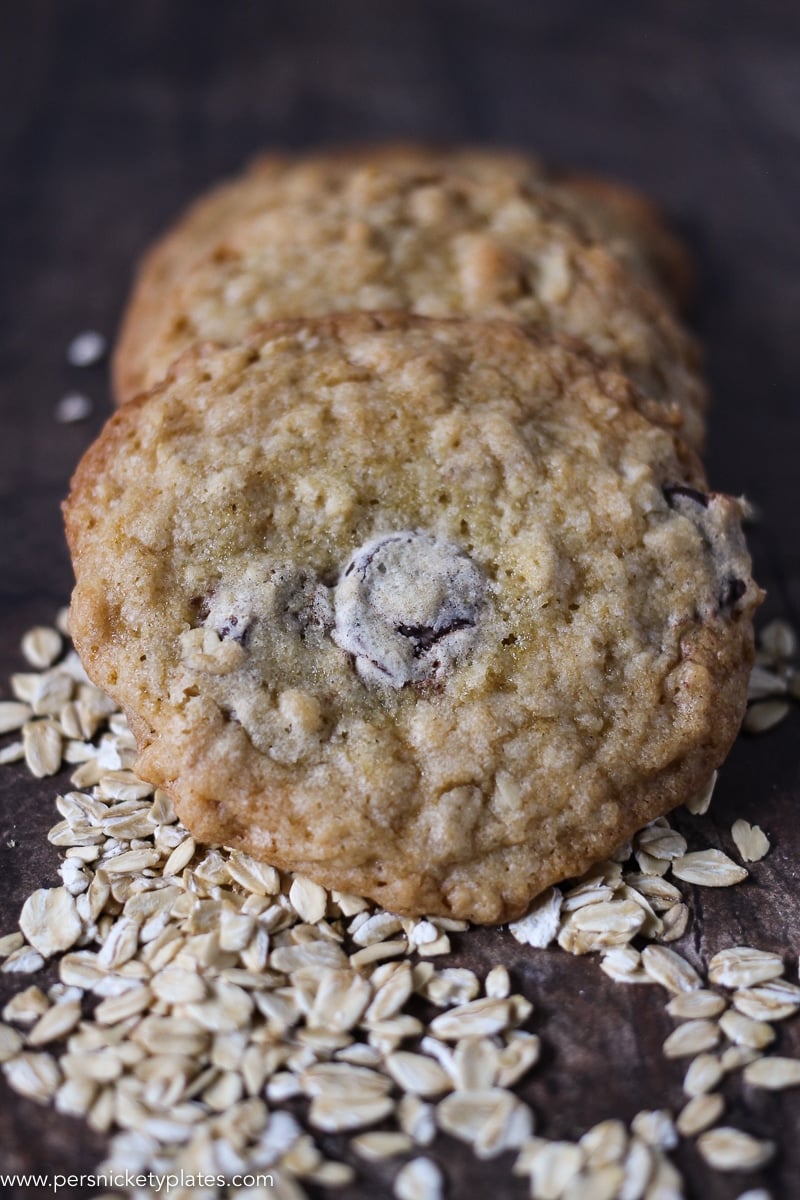 three ranger cookies on a dark wood table and spilled oats