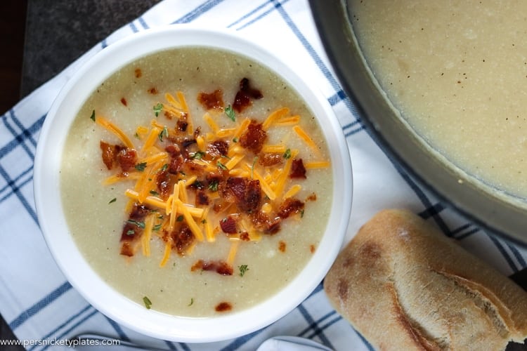 bowl of loaded potato soup with pot of soup and chunk of bread