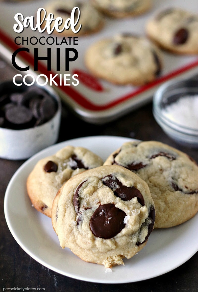 three Salted Chocolate Chip Cookies on a white plate with extras on a baking sheet