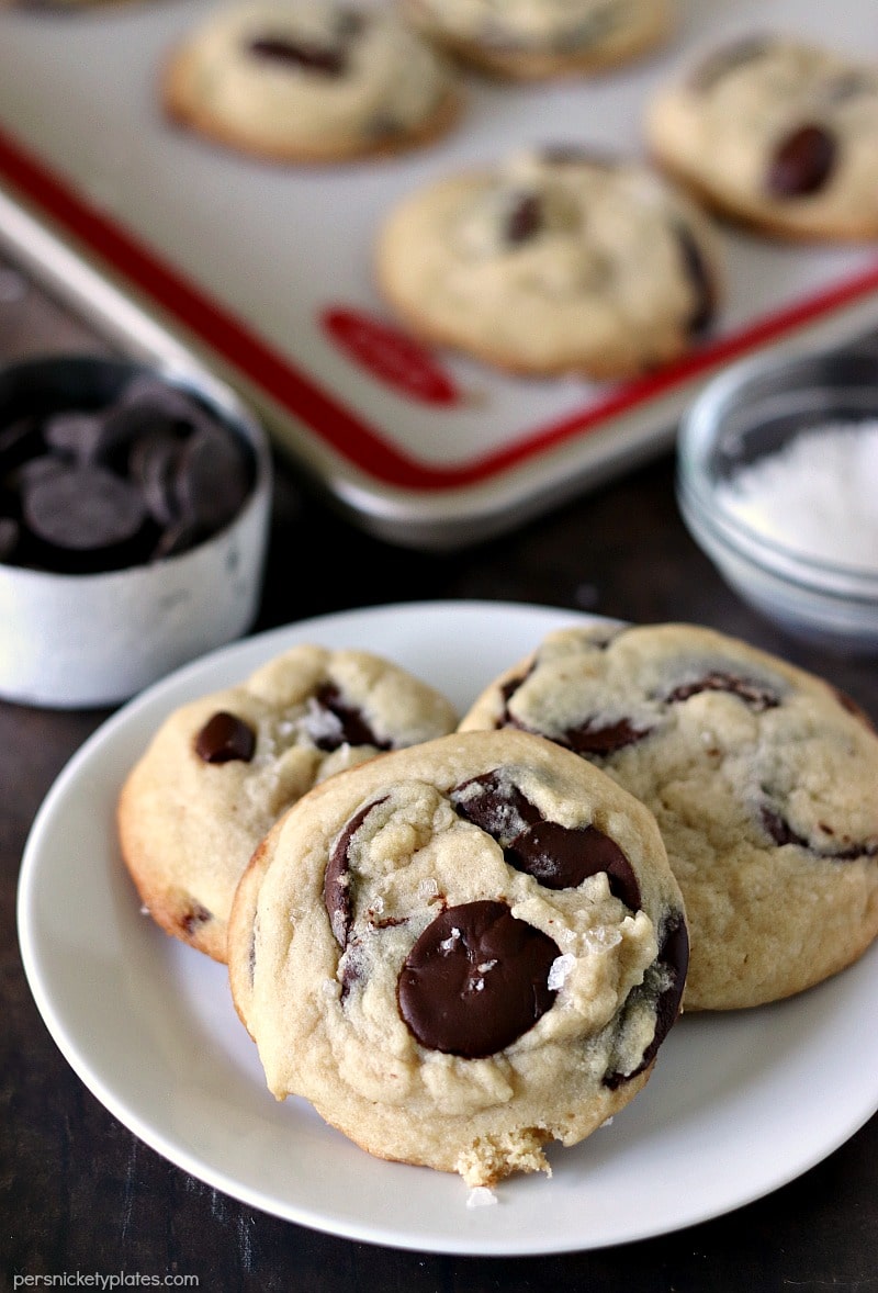 closeup of three Salted Chocolate Chip Cookies with a baking sheet of more cookies in the background