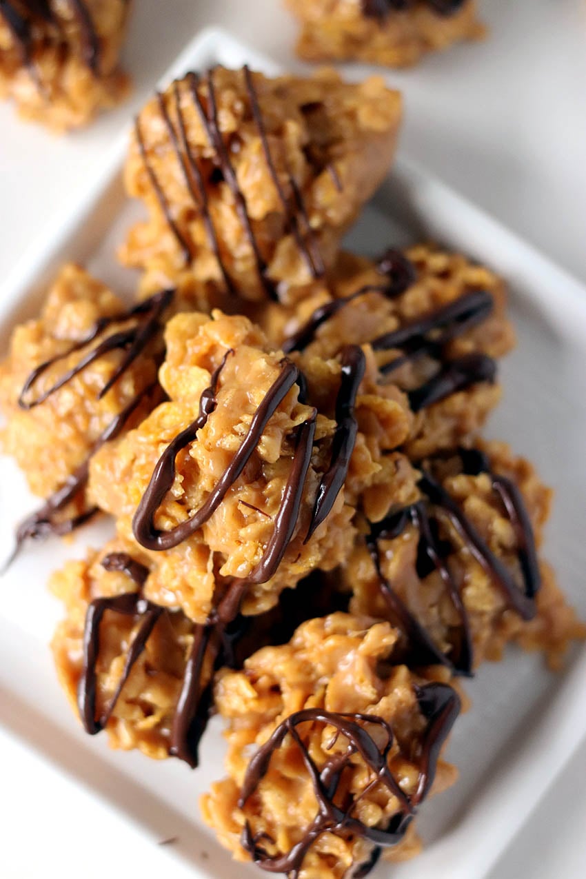 stack of chocolate peanut butter cornflake cookies on a white plate platter of cornflake cookies drizzled with chocolate.