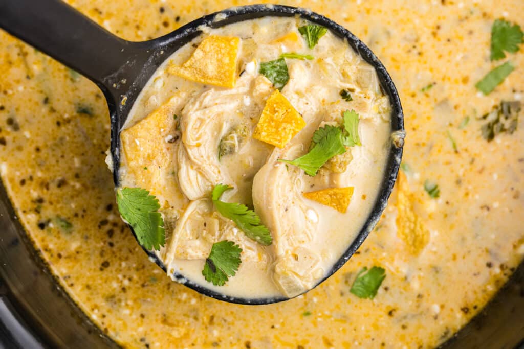 ladle lifting green enchilada soup from a crockpot.
