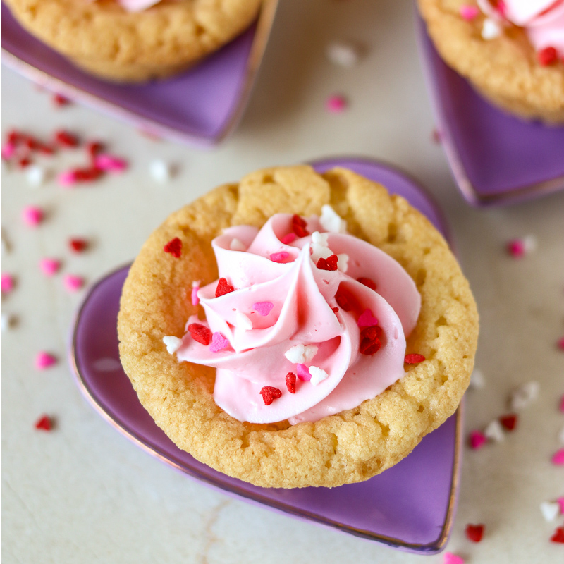 Valentine Sugar Cookie Cups are a simple, semi-homemade treat that you can whip up in no time! A sugar cookie base filled with pink frosting and topped with Valentine sprinkles. | www.persnicketyplates.com