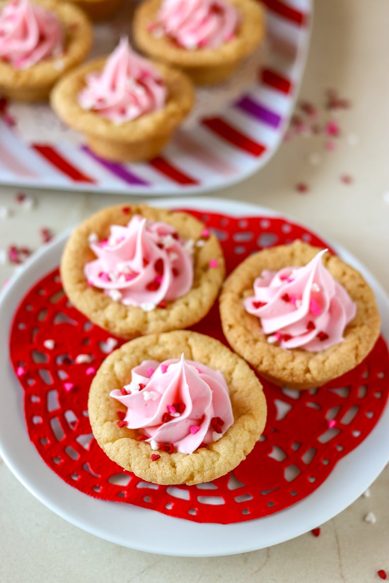 Valentine Sugar Cookie Cups are a simple, semi-homemade treat that you can whip up in no time! A sugar cookie base filled with pink frosting and topped with Valentine sprinkles. | www.persnicketyplates.com