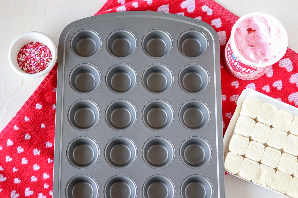 Valentine Sugar Cookie Cups are a simple, semi-homemade treat that you can whip up in no time! A sugar cookie base filled with pink frosting and topped with Valentine sprinkles. | www.persnicketyplates.com
