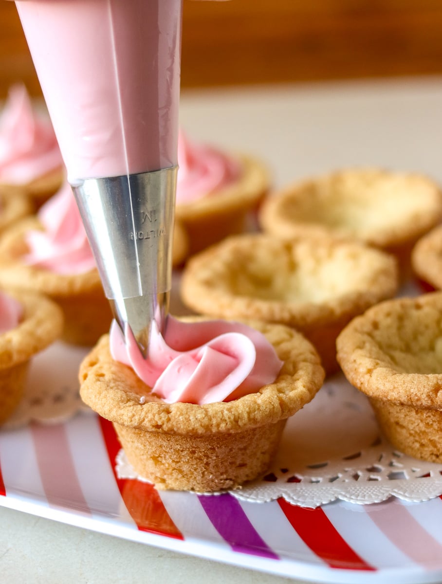 Valentine Sugar Cookie Cups are a simple, semi-homemade treat that you can whip up in no time! A sugar cookie base filled with pink frosting and topped with Valentine sprinkles. | www.persnicketyplates.com