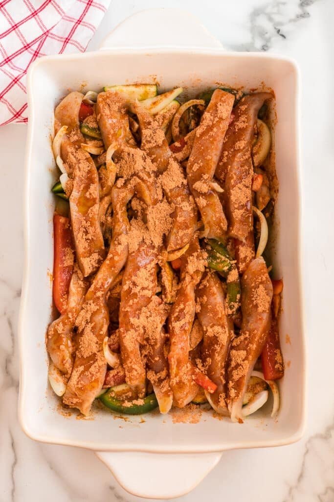 overhead shot of seasoned chicken and veggies in a baking dish.