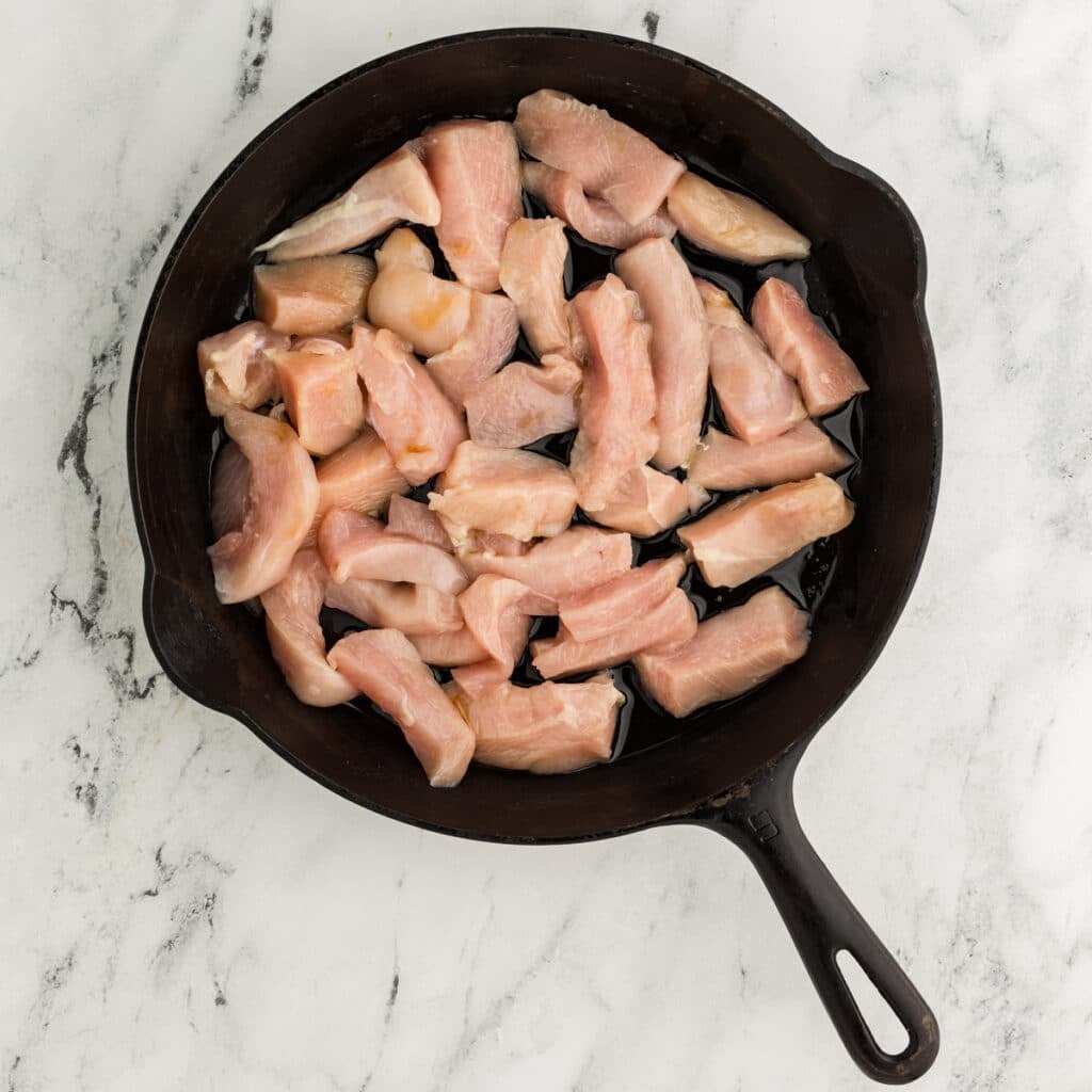overhead shot of raw chicken pieces in a cast iron skillet.