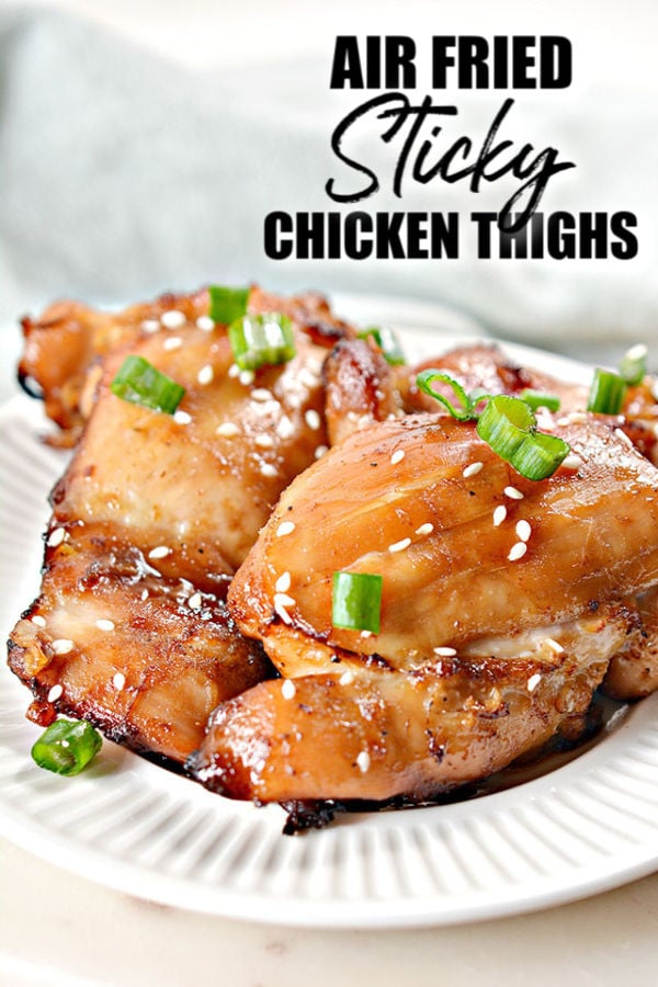 air fried sticky chicken thighs on a white plate with green onion & sesame seed garnish