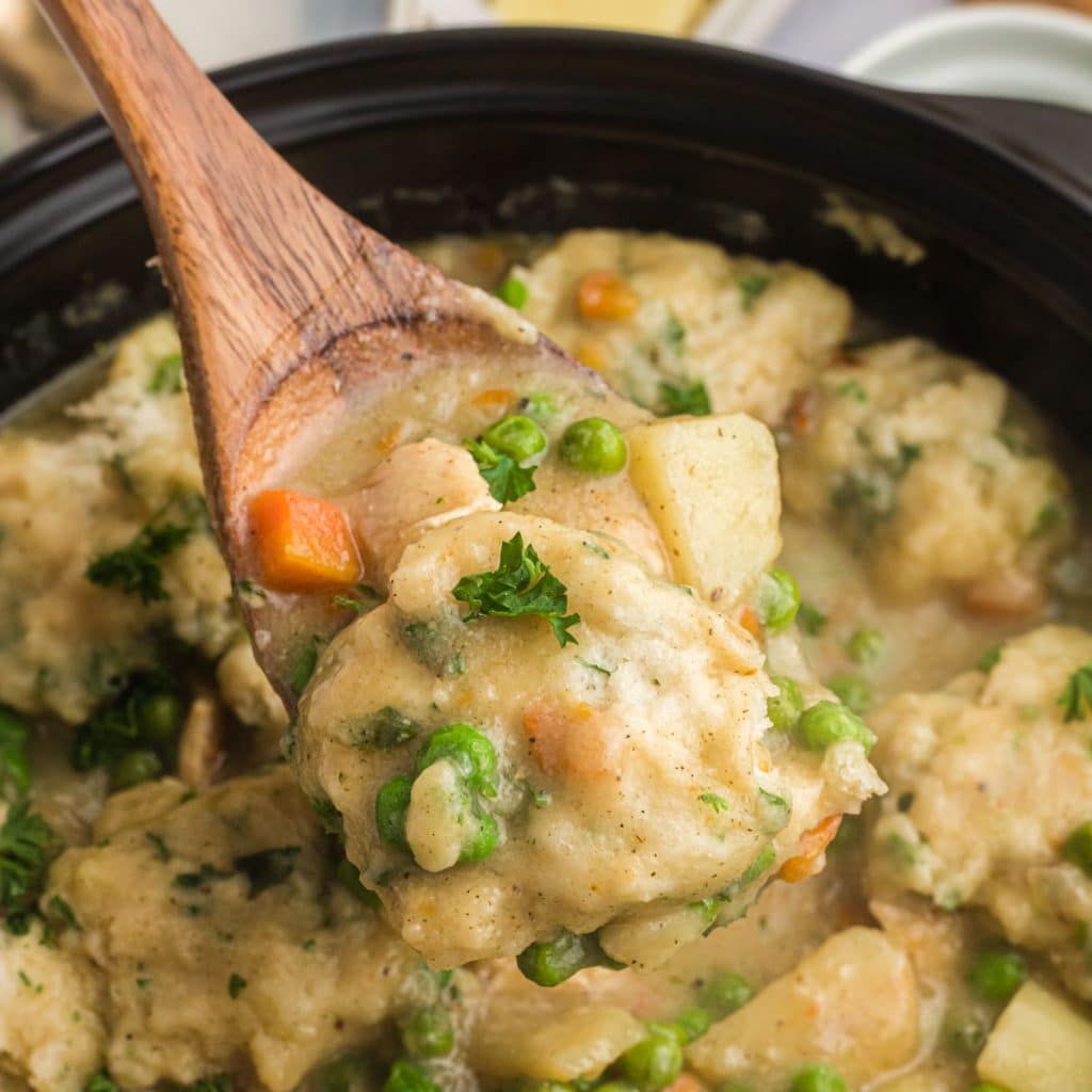 wooden spoon lifting a scoop of chicken and dumplings out of a pot.