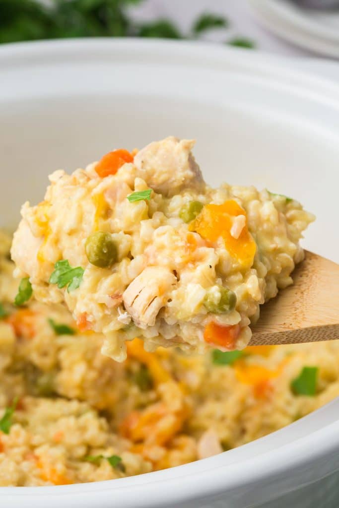 a wooden spoon lifting a scoop of chicken and rice from a crockpot.