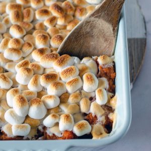 wooden spoon dipping into sweet potato casserole topped with marshmallows