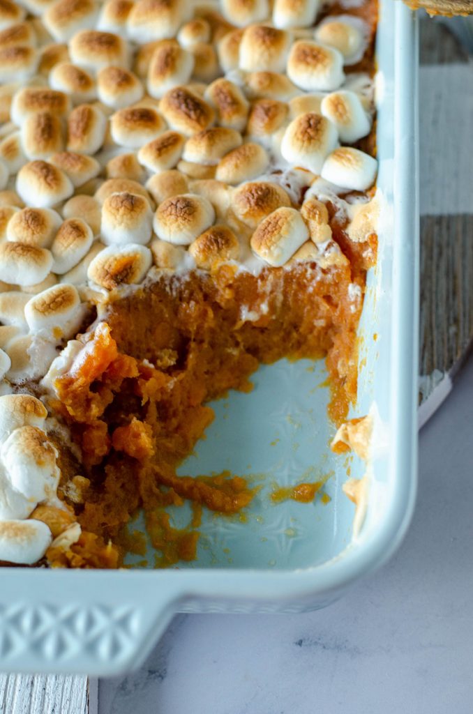 close up of baking dish with scoop of sweet potato casserole missing