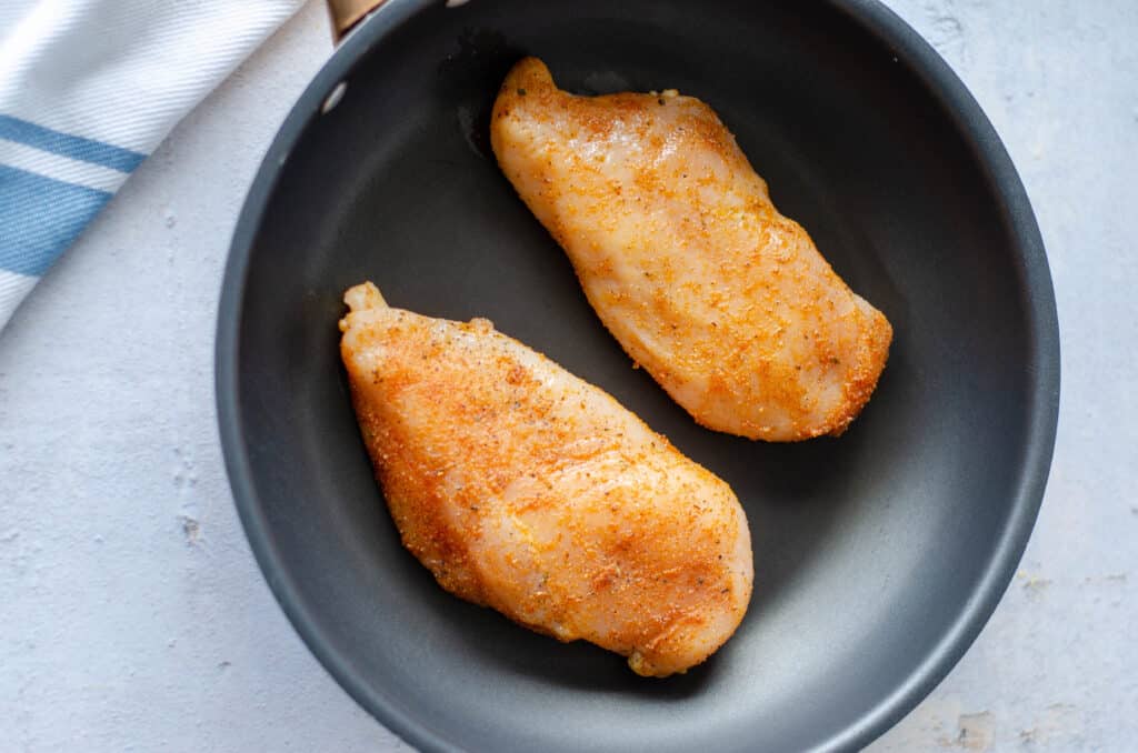 two seasoned chicken breasts in a skillet.