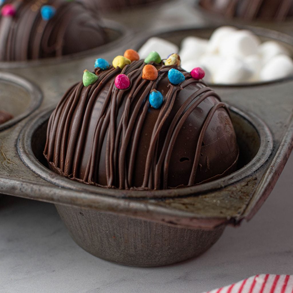 hot chocolate bomb in a cupcake tray topped with rainbow chips