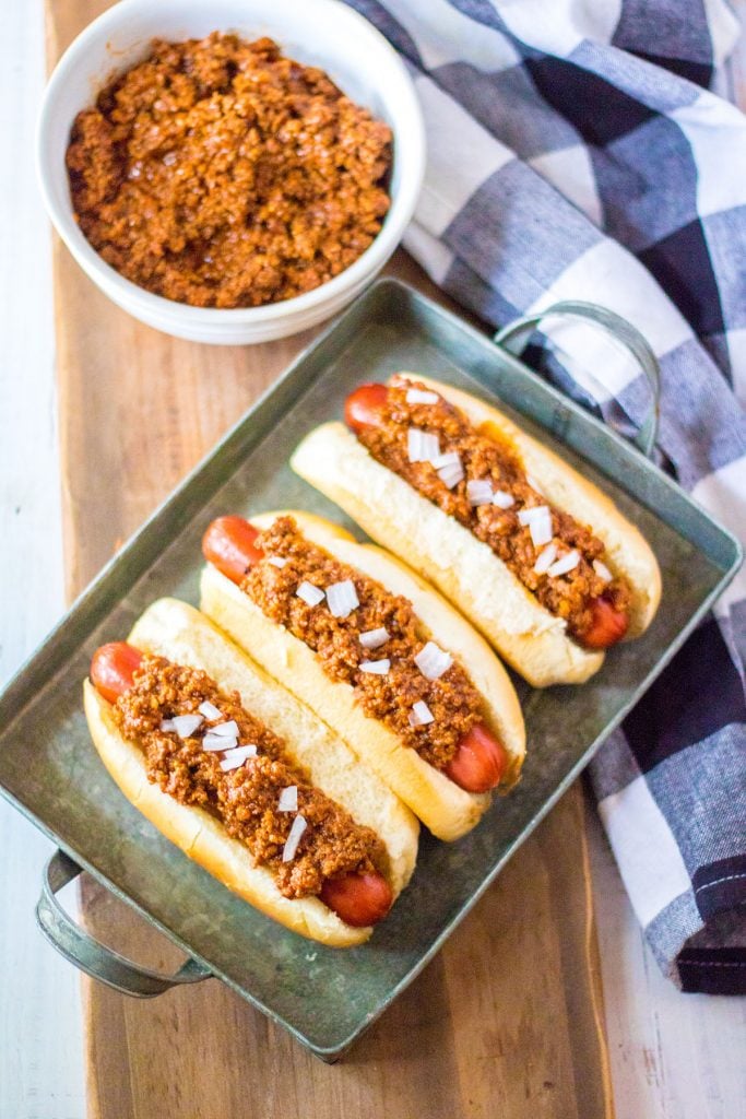 overhead shot of 3 hotdogs on a tray topped with chili & onions