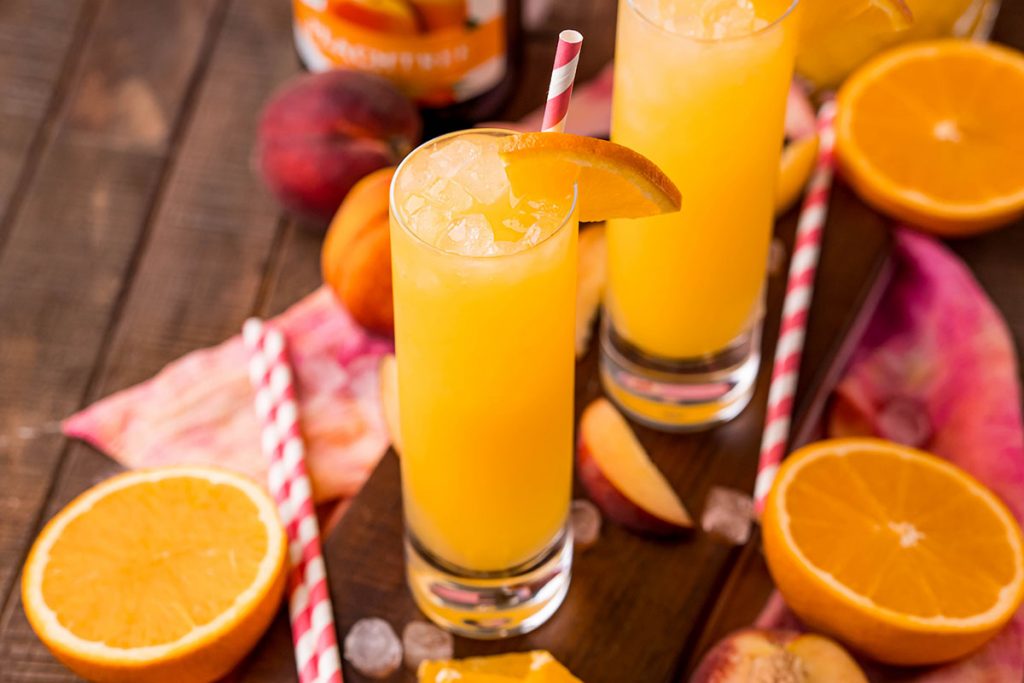 fuzzy navel cocktail surrounded by oranges & peaches