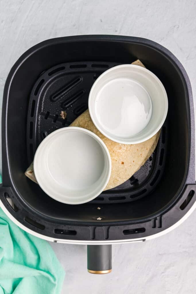 two ramekins weighing down a quesadilla in an air fryer.