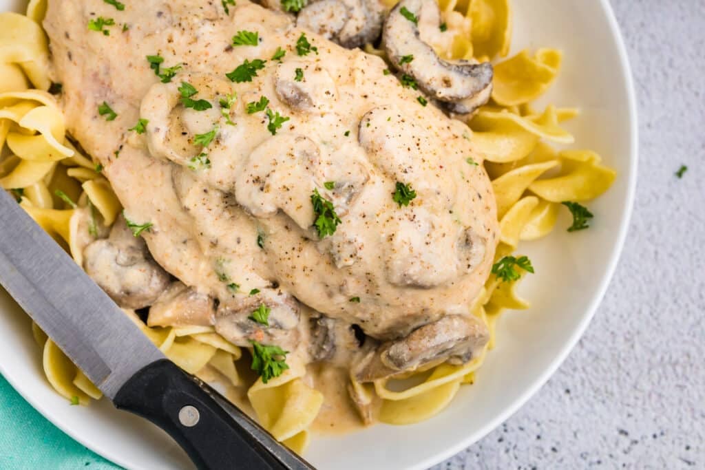 creamy mushroom chicken over egg noodles on a white plate with a knife.