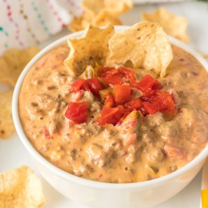 white bowl of rotel dip topped with tomatoes and chips stuck in