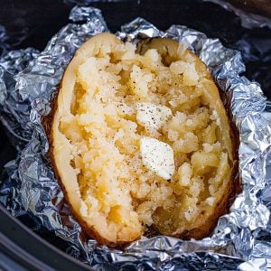 baked potato in foil split open with butter sitting in a slow cooker
