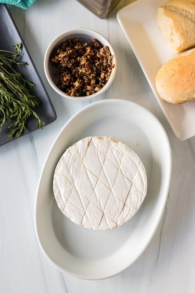 brie in a baking dish, scored & ready to be topped for baking