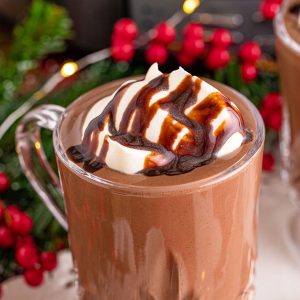 hot chocolate in a glass mug topped with whipped cream and chocolate sauce