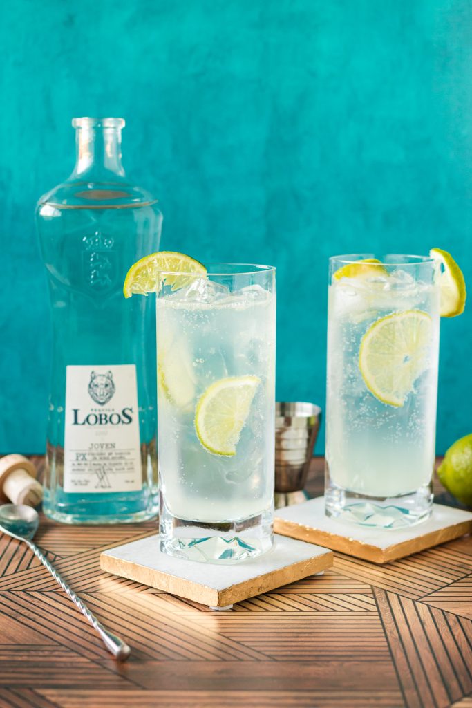 two cocktails with lime wedges next to a bottle of lobos tequila