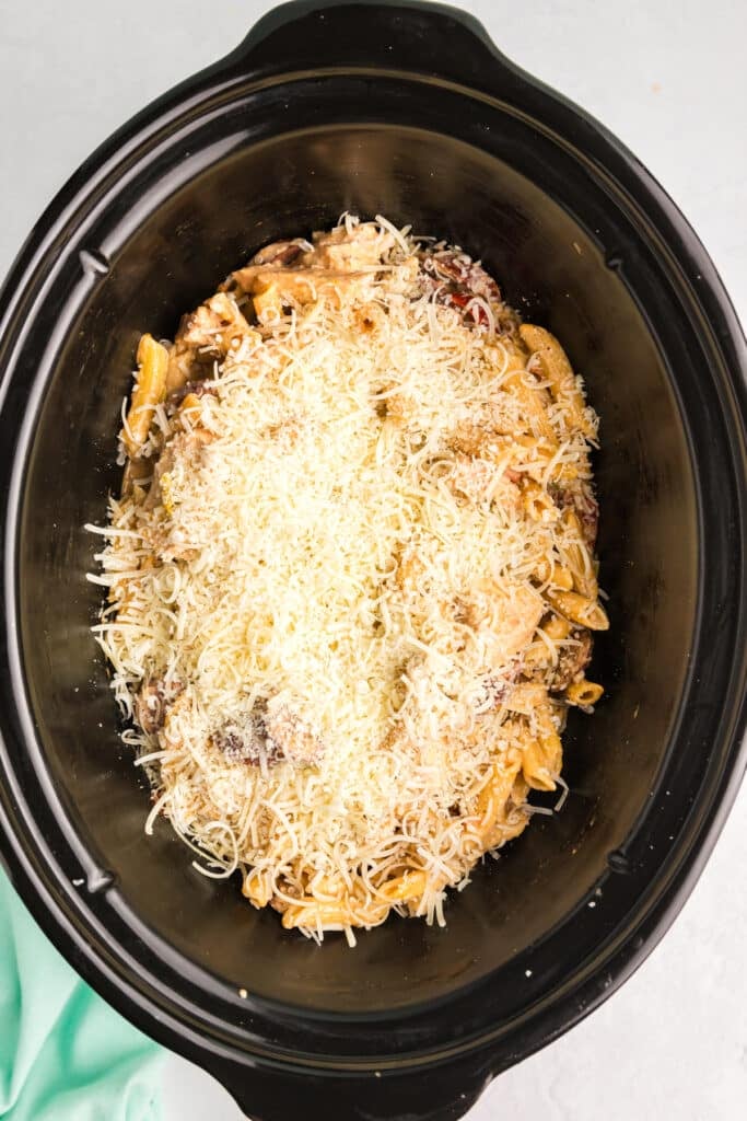 parmesan cheese sprinkled over pasta in a slow cooker.