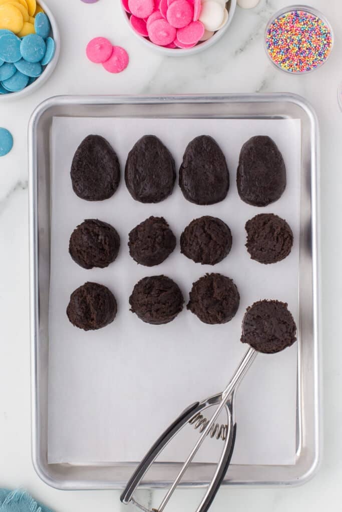 cookie scoop laying on a baking sheet with oreo truffles.
