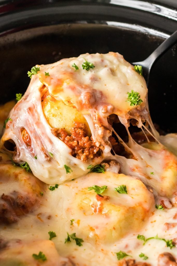 spoon lifting cheesy ravioli from a crockpot.
