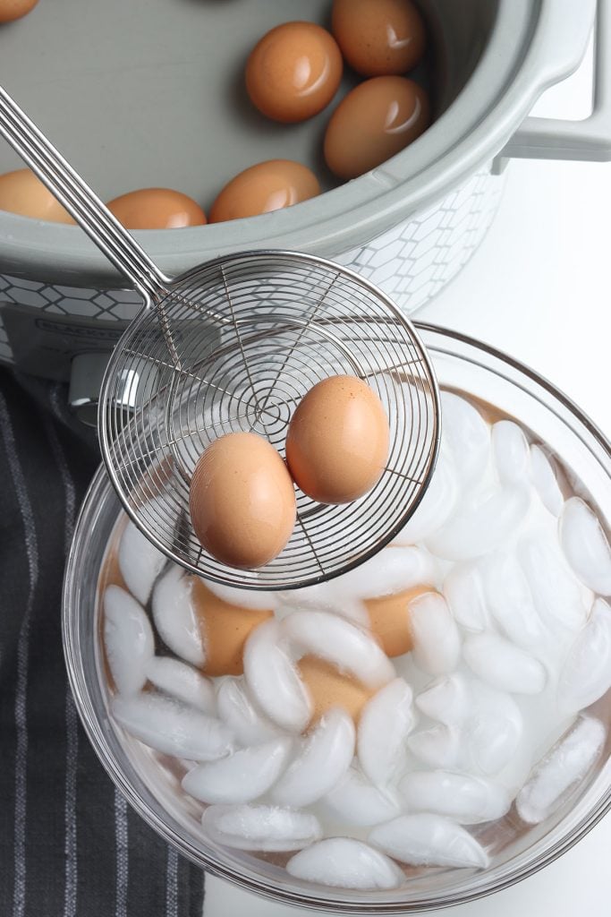 strainer lifting hard boiled eggs from an ice bath.