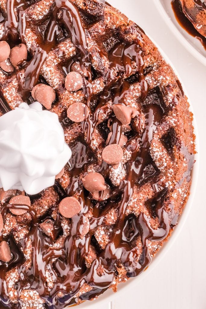 closeup overhead shot of chocolate waffles topped with chocolate chips, chocolate syrup, and whipped cream.