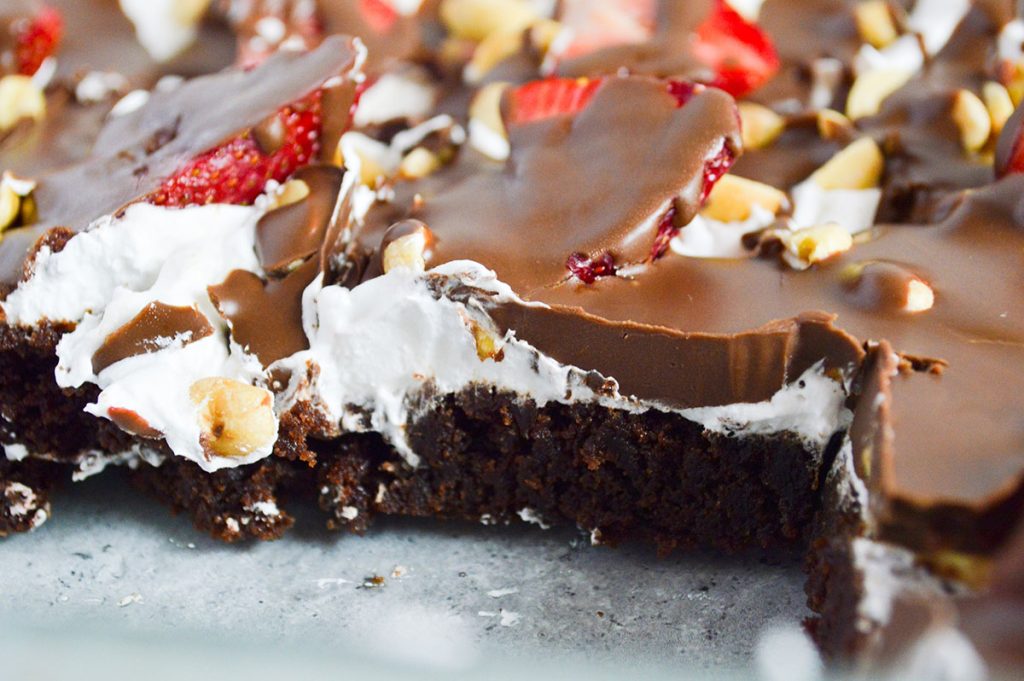 side view of layered brownie, whipped cream, & strawberry delight topped with chocolate.