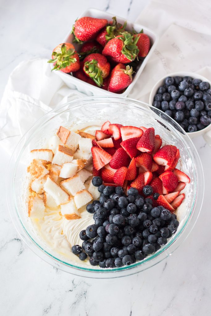 overhead shot of strawberries, blueberries, and cubes of angel food cake in a glass bowl.