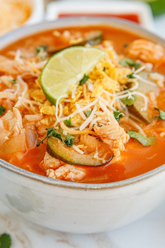 closeup of on the border copycat chicken tortilla soup topped with cheese and lime.