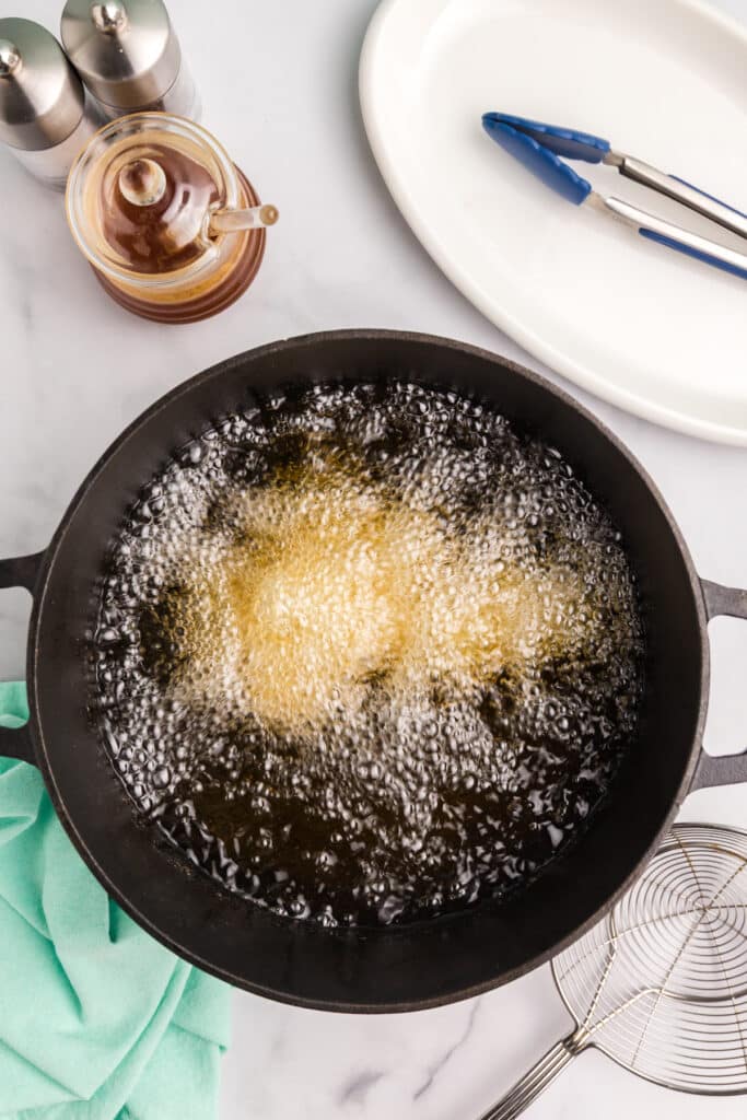 Chicken nuggets frying in bubbling oil in a cast iron pan.