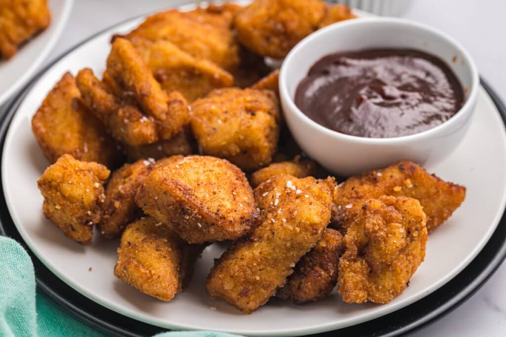 Plate of crispy chicken nuggets served with barbecue dipping sauce.