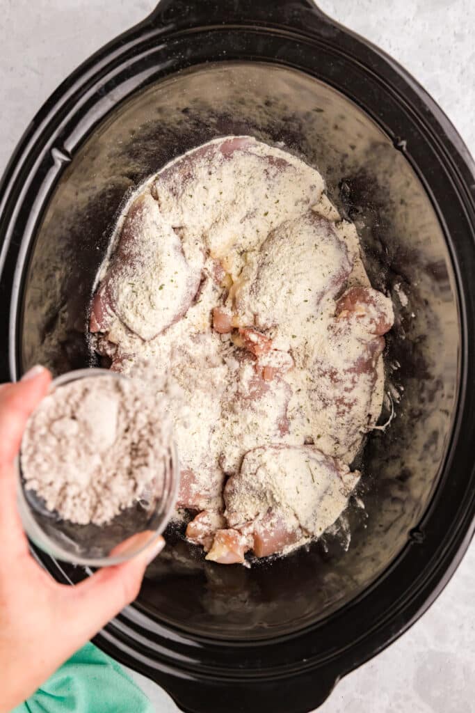 gravy mix sprinkling over chicken in a crockpot.