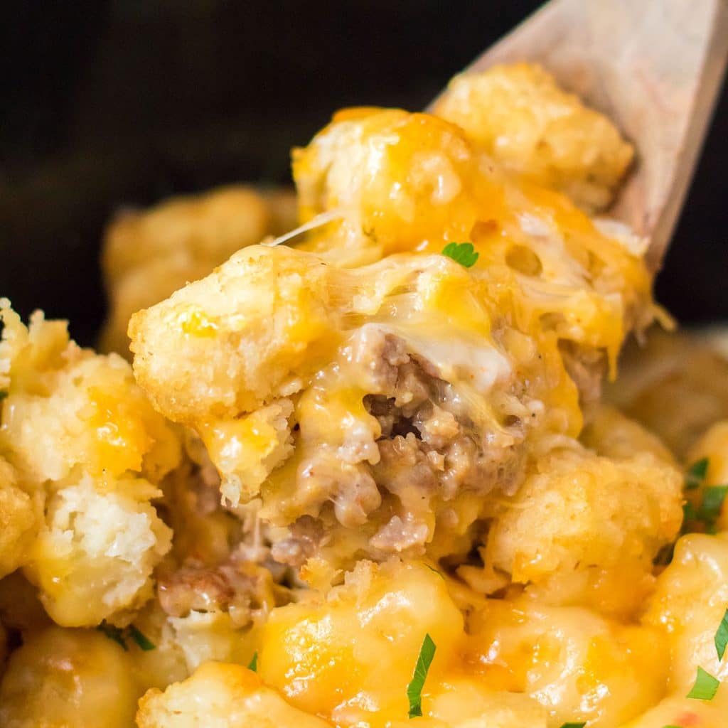 wooden spoon dipping into cheesy tater tot casserole in a crockpot.