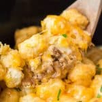 wooden spoon dipping into cheesy tater tot casserole in a crockpot.