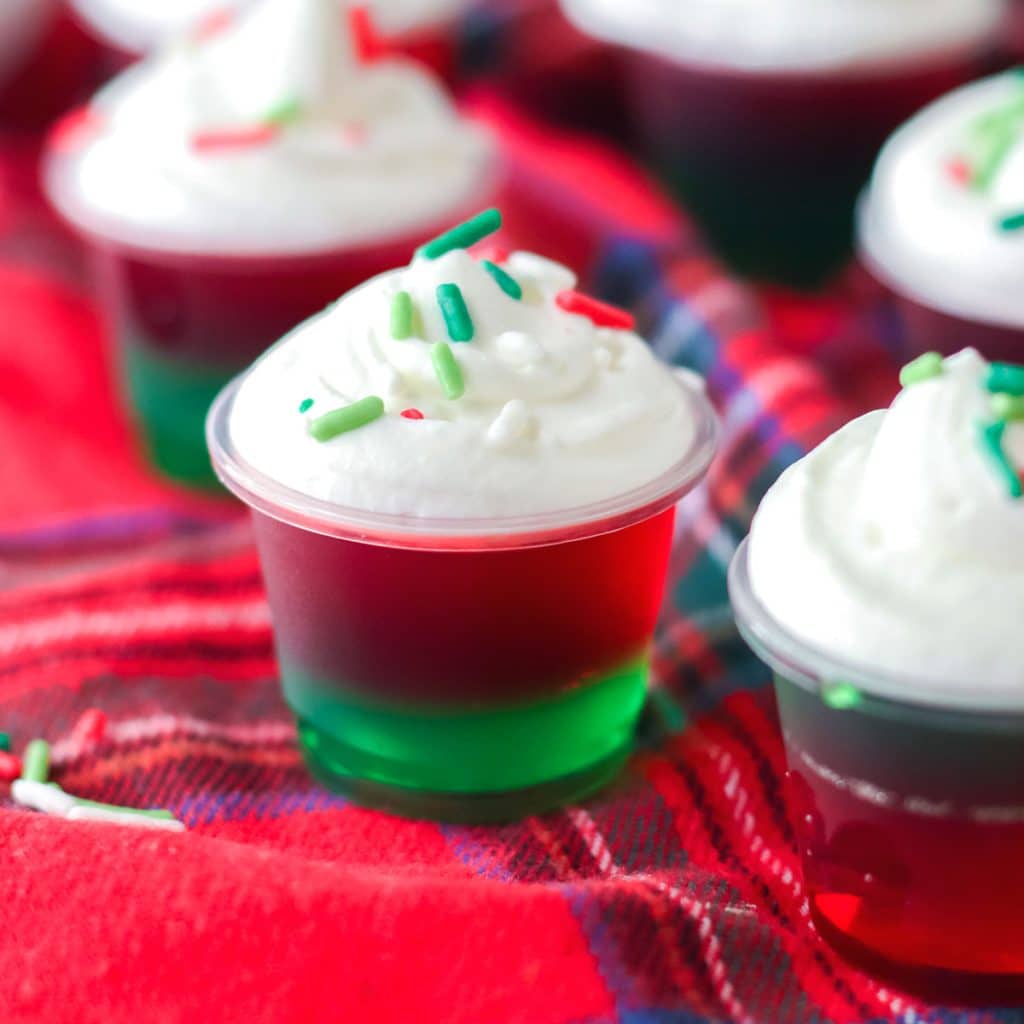 red & green christmas jello shot topped with whipped cream & sprinkles.