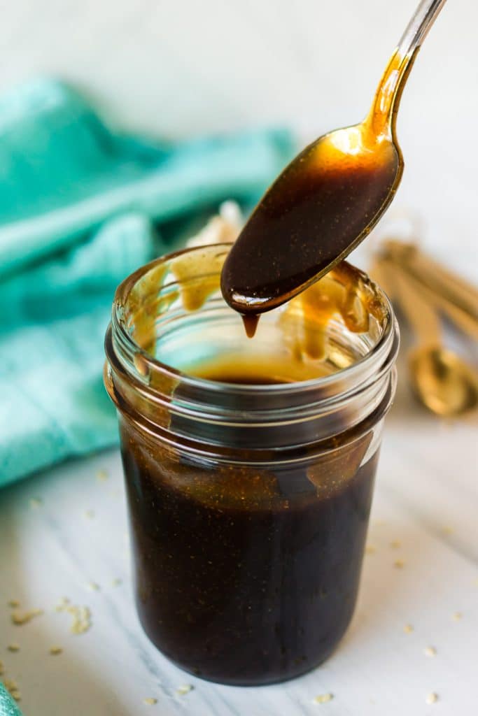 spoon lifting teriyaki sauce from a glass jar.