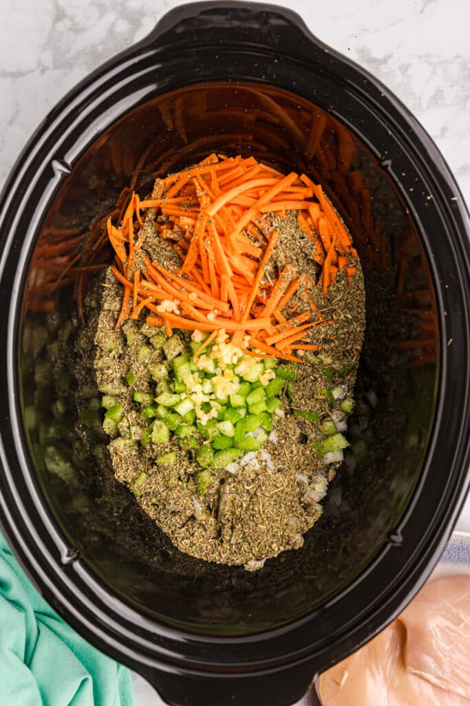 overhead shot of diced celery, grated carrots and seasonings in a crockpot.