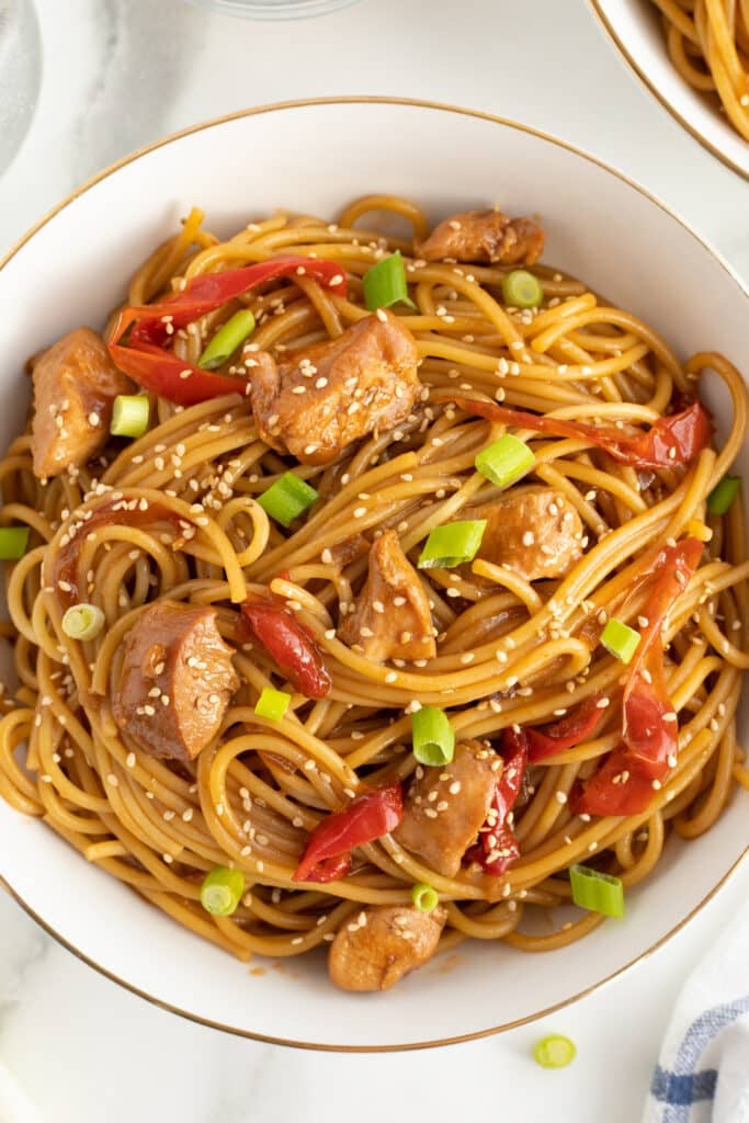 overhead shot of chicken, noodles, red peppers, and scallions in a bowl.