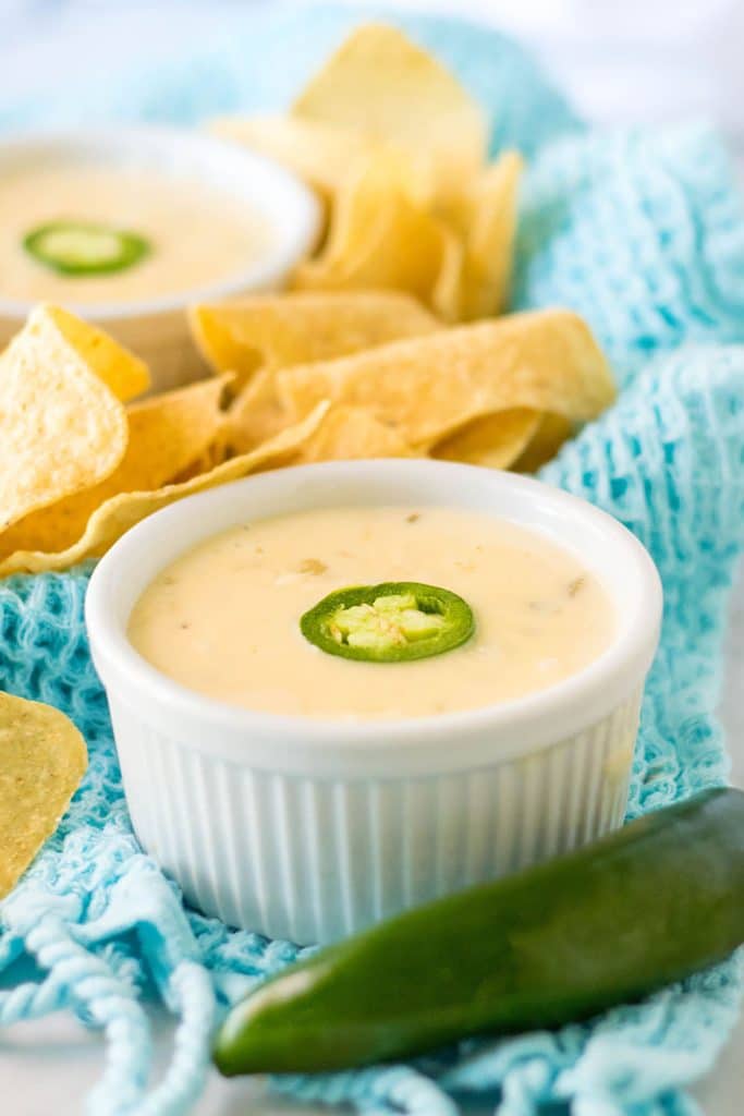 white bowl of queso next to a jalapeno.
